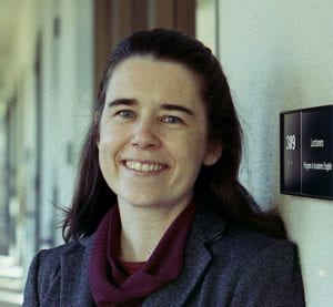 Picture of a white woman with long dark hair, smiling, wearing a sweater and blazer.